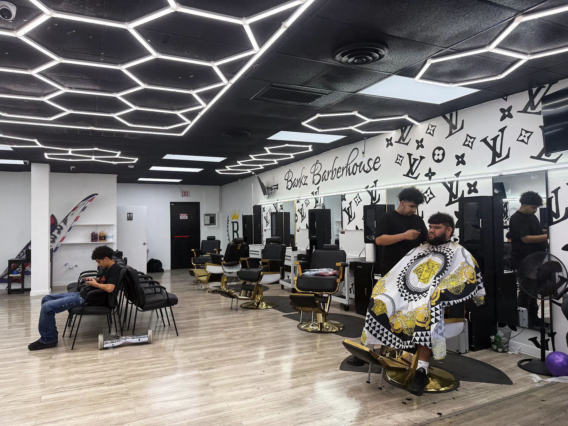 Inside Bankz BarberHouse — hexagon lights, gold chairs, and the LV monogram wall
